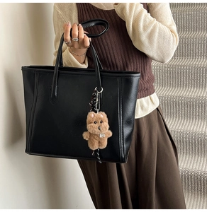 Detail of black tote bag with leather texture and brown plush bear charm pendant