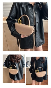 Detail of beige saddle bag featuring a gold round handle and adjustable shoulder strap