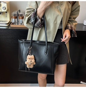 Detail of a black large tote bag with leather texture and cute brown plush puppy charm
