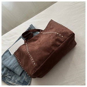 Detailed side view of deep brown suede tote bag with silver rivet studs on white fabric