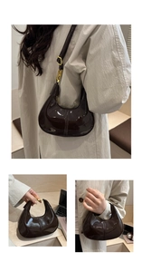 Detail view of a dark brown patent leather hobo bag featuring shiny gold metal buckle