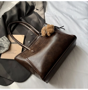 Detail of a brown vintage tote bag with pebble texture and plush bear charm decoration