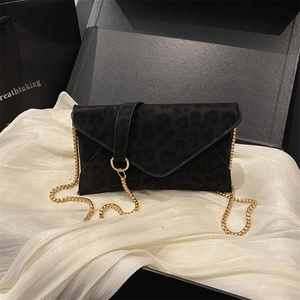 Sac enveloppe noir à motif léopard avec chaîne dorée sur fond de soie blanche satinée