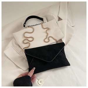 Macro detail of black suede envelope bag with gold ball chain on beige blazer