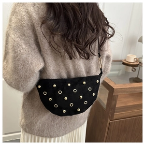Détail du sac demi-lune en daim noir avec clous et anneaux dorés dans un cadre de vie