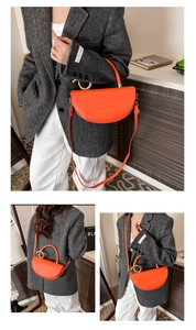 Detail of bright orange half-moon bag featuring a large gold metal ring handle and logo
