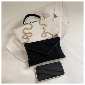 Detail view of black suede envelope clutch with gold chain on a beige blazer background