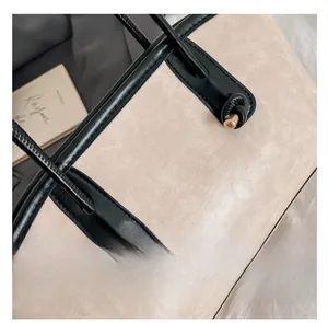 Macro detail of beige matte tote bag with black leather handle and gold metal accents