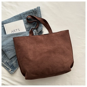 Detail view of large brown suede tote bag on soft bedding with artistic accessories