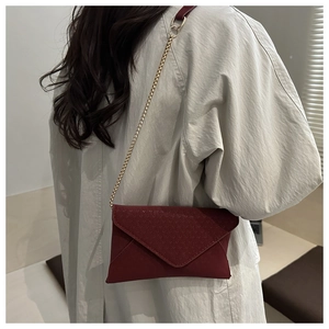 Detail of dark red envelope crossbody bag with gold chain strap on model's shoulder