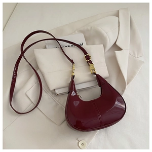 Gros plan d'un sac demi-lune en cuir verni bordeaux sur un costume blanc chic