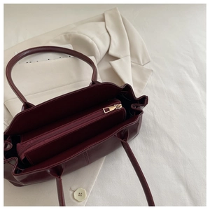 Detail view of burgundy handbag featuring interior gold zipper and leather texture