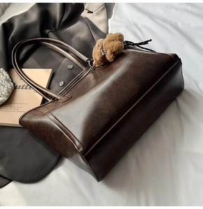 Detail of dark brown vintage faux leather tote bag with a cute plush bear pendant