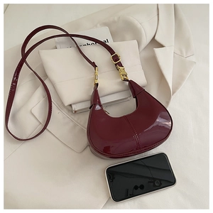 Detail view of burgundy patent leather half-moon bag with gold zipper and hardware