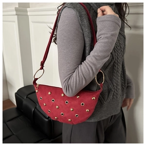 Détail du sac croissant en daim rouge avec clous dorés et œillets sur modèle