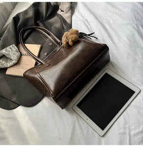 Detail of vintage brown tote bag with bear charm on a bed with lifestyle accessories