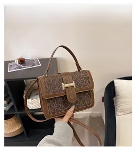 Détail d'un sac carré marron avec monogramme, boucle en métal doré et poignée en cuir