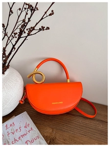 Détail du sac selle orange en similicuir avec anneaux dorés et logo imprimé