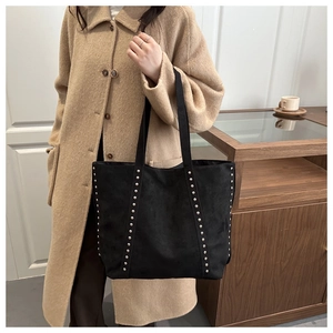 Detail of matte black tote bag with silver rivets carried by model in a wool coat