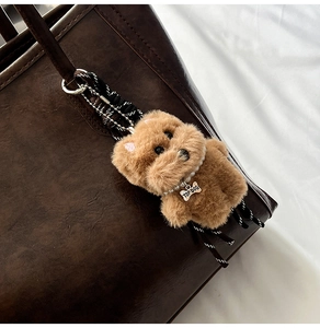 Plush dog keychain with pearl necklace and bone tag on a brown leather tote bag