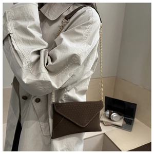 Detail of dark brown envelope crossbody bag with grainy texture and gold chain strap