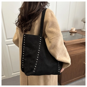 Detail of black suede tote bag with silver studs on shoulder strap in home setting