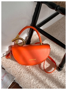 Détail du sac demi-lune en cuir orange avec de gros anneaux dorés sur le tapis