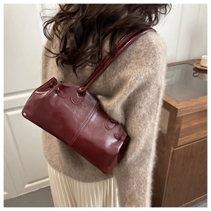 Burgundy glossy leather baguette bag worn over the shoulder by a model in a cozy fall outfit