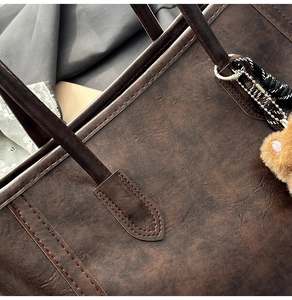 Detail of dark brown leather tote bag with fine stitching and plush charm accessory