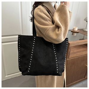 Detail of black suede tote bag with silver rivet studs worn by model in a cozy room