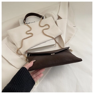 Detail of dark brown envelope clutch bag featuring gold chain and soft leather texture
