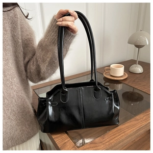 Detail of a black glossy PU leather baguette bag with thin straps and vertical stitching