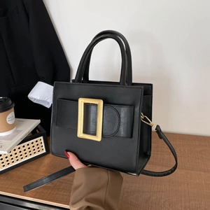 Classic black leather rectangular handbag with gold buckle on wooden desk setting