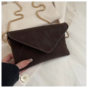 Detail of dark brown envelope crossbody bag with gold chain strap and leather texture