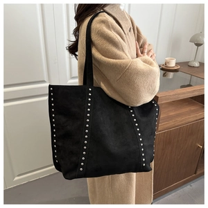 Detail of a black suede tote bag with silver studs worn on a shoulder for daily use