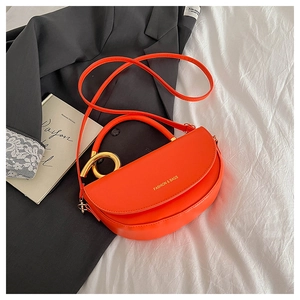Détail d'un sac selle orange avec poignée dorée posé sur un blazer gris