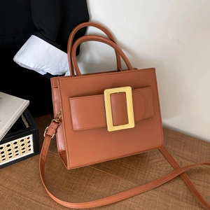Vintage brown leather tote bag with large gold buckle on a stylish wooden desk