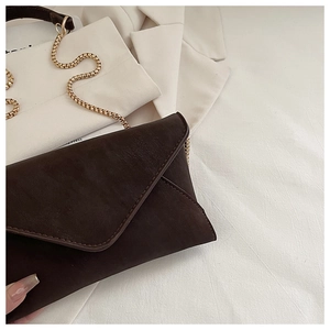 Detail of dark brown leather envelope clutch bag with elegant gold snake chain strap