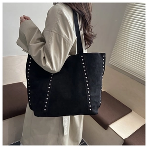 Detail of black suede tote bag with silver rivets and wide strap shown on a model