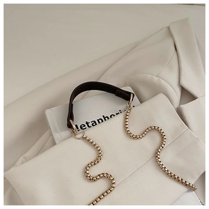 Detail view of light gold block chain strap and dark brown leather shoulder pad accessory