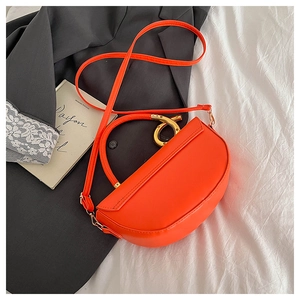Détail du sac selle orange avec poignée dorée sur fond de blazer gris foncé