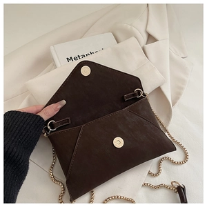 Detail of dark brown suede envelope bag featuring a gold chain and magnetic snap closure