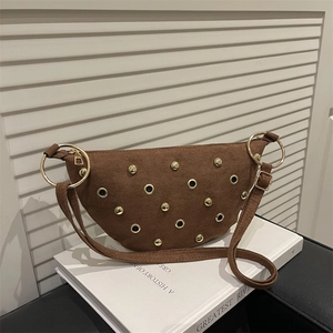 Sac demi-lune en daim marron avec clous dorés et anneaux sur un livre blanc