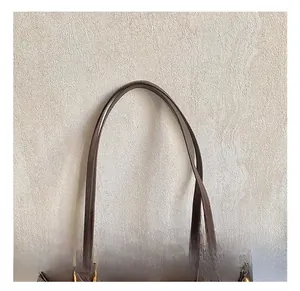 Detail of dark brown leather tote handle with gold ring buckle and precise stitching