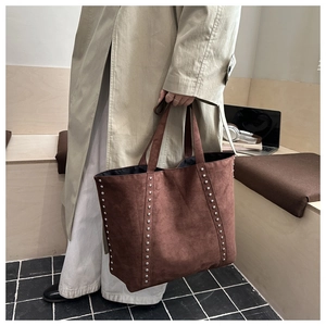 Detail of vintage brown suede tote bag with silver studs held by a model in a minimalist room