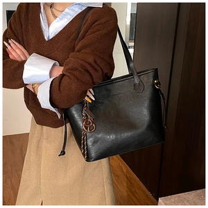 Detail of a large black leather tote bag featuring a decorative brown knotted bag charm