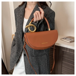 Détail d'un sac selle marron avec poignée en métal et lettrage doré tendance