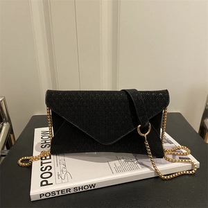 Elegant black woven envelope bag with gold chain strap displayed on a white art book