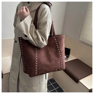 Close-up of brown suede tote bag with silver rivets worn over a beige trench coat
