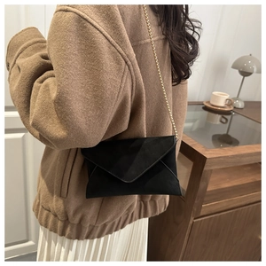 Detail of black suede envelope crossbody bag with a slim gold chain strap on a model
